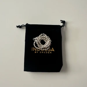 Silverfärgat halsband från Indossa - Stilrent silverfärgat halsband från Indossa med en tvinnad design. Halsbandet är 50 cm långt och 3 mm tjockt. Levereras i en snygg svart påse med Indossa-logga. Nypris 400, mitt pris, 200kr