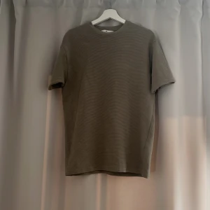 Typ oliv grön randig/sträckig t-shirt - Säljer en T-shirt som aldrig har använts, Materialet känns mjukt och bekvämt mot huden. Pris kan diskuteras