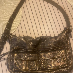 Svart axelväska från BDG - Säljer en snygg svart axelväska från BDG i skinn, men köpt på Urban outfitter. Väskan har två framfickor med knappar och en dragkedja upptill. 🙏