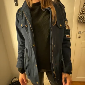 Mörkblå jacka med pärldetaljer - Snygg mörkblå jacka med unika pärldetaljer på ärmen. Jackan har dragkedja och knappar framtill samt praktiska fickor. Perfekt för en cool och avslappnad stil.