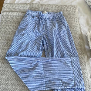 Blå- och vitrandiga byxor från Arket - Säljer ett par blå- och vitrandiga byxor från Arket. Byxorna har en bekväm passform med elastisk midja och knytband. Perfekta för en avslappnad stil. Nypris 700 och ej använda