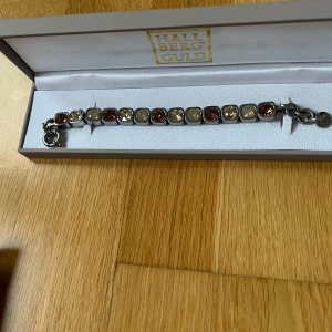 Armband från DYRBERG/KERN - Snyggt armband i silver från  DYRBERG/KERN med glittriga stenar i olika nyanser av brunt och brunt. Säljer den för 370 kr, nypris 1149 kr. Armbandet har en robust kedja och en säker låsning. Perfekt för att ge en touch av elegans till din stil.