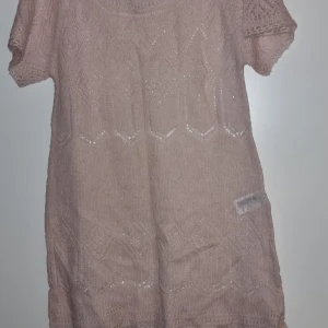 Ljusrosa stickad hålmönstrad  klänning, st S - Söt ljusrosa stickad klänning med korta ärmar och ett fint hålmönster. Perfekt för en avslappnad och stilren look. Klänningen har en rund hals och är gjord i ett mjukt material.