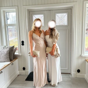 Champagnefärgad bal klänning - En champagnefärgad långklänning i satin med v-ringning och smala axelband. Klänningen har en slits på sidan och en öppen rygg. Använde en gång på min bal men säljer nu för andra som kanske vill använda den i samma syfte eller annat tillfälle! 🩷Jag står till vänster på bilden och är 165 cm lång. Klänningen är i st 38 men sitter som en S. Ordinarie pris: 774 kr