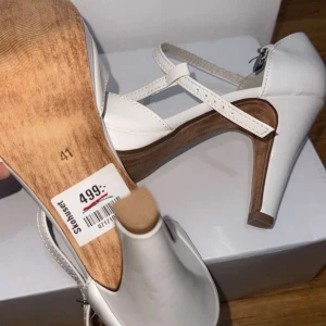 Vita klackskor med remmar - Snygga vita klackskor från Rieker med elegant remdesign och bekväm klack. Perfekta för en stilren look.