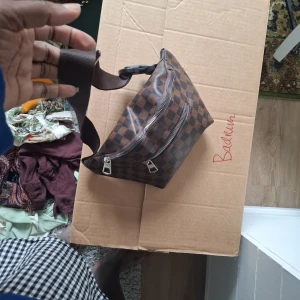 Brun rutig magväska med dragkedjor - Säljer en brun magväska med klassiskt rutigt mönster och två dragkedjefack. Väskan har justerbart band och är perfekt för att bära det viktigaste. Snygg accessoar som passar till många outfits.