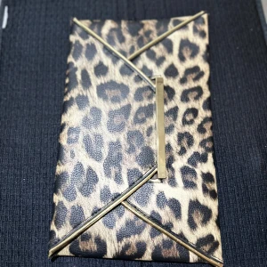 Leopardmönstrad kuvertväska med gulddetaljer - Säljer en snygg kuvertväska med leopardmönster och stilrena guldfärgade detaljer. Väskan har ett brunt innerfoder och ett mindre innerfack. Perfekt accessoar för att lyfta din outfit!