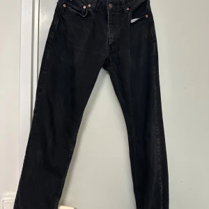 Svarta Levis 501 jeans - Klassiska svarta Levis 501 jeans med raka ben och knappgylf. Jeansen har fem fickor och den ikoniska Levis-lappen bak i midjan. Perfekta för dig som gillar en tidlös och clean look.
