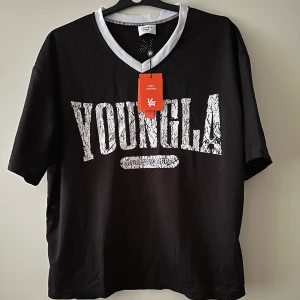 YoungLa, VARSITY FOOTBALL CROPPED JERSEY - Svart mesh t-shirt från YoungLA med vit kontrastkrage och stor vit text 'YOUNGLA' framtill. T-shirten har korta ärmar och sportig känsla, perfekt för träning eller chill. Snygg och luftig design med modern passform.