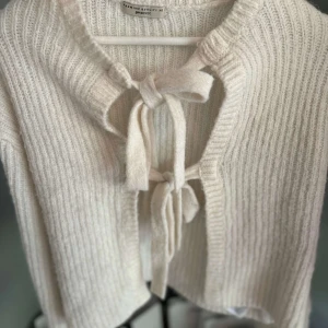 Vit stickad kofta med knyt från Gina Tricot - Superfin vit stickad kofta från Gina Tricot med två knyt framtill. Koftan har lång ärm och ribbad struktur, perfekt för lager-på-lager. Enkel och stilren design som passar till mycket.
