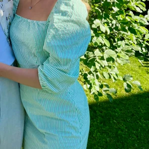 Grön- och vitrandig klänning från C.W. - Superfin grön- och vitrandig klänning från C.W. med puffärmar och fyrkantig ringning. Klänningen har trekvartsärm. Perfekt för sommarens alla tillfällen!