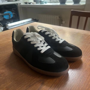 Svarta sneakers med vit sula och snörning - Säljer ett par stilrena svarta sneakers med vit sula och vita skosnören. Skorna har en klassisk design med rund tå och platt sula, perfekta för en avslappnad look. Passar till många olika outfits och är riktigt bekväma. Skriv om ni har några frågor
