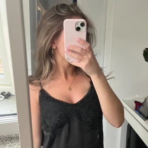 Svart satintopp med spetsdetaljer - Säljer en svart satintopp med tunna axelband och vacker spets upptill. Toppen har en lätt glansig finish och är perfekt för att skapa en stilren look. Aldrig använd!💓