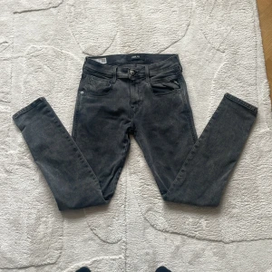 Replay Anbass Hyperflex jeans i grå denim - Säljer ett par Replay Anbass Hyperflex jeans i grå tvätt. Slim fit-modell med klassisk femficksdesign och dragkedjegylf. Tillverkade i återvunnen stretchig denim för extra komfort och rörelsefrihet.
