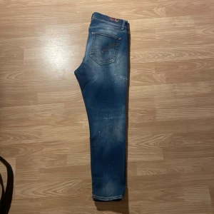 Blå superskinny jeans från Dondup - Säljer ett par blå jeans från Dondup, modell Alex Superskinny Fit. Jeansen har slitna detaljer och små färgstänk, klassisk femficksdesign och dragkedjegylf. Perfekta för dig som gillar en trendig look. Kan gå ner lite vid snabb affär