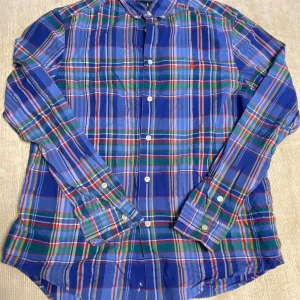 Blårutig skjorta från Ralph Lauren - Säljer en klassisk blårutig skjorta från Ralph Lauren med lång ärm och knappar framtill. Skjortan har broderad logga på bröstet och är tillverkad i bomull med lite stretch. Perfekt för dig som gillar färg och mönster! Denna är liten i storleken men hör av er om ni undrar något!