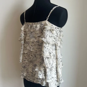 Blommig volangtop från Truly by Part Two - Säljer en luftig och somrig blommig volangtop från Truly by Part Two i 100% siden. Toppen är krämvit med mönster och har justerbara axelband.