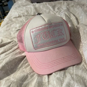 Rosa keps från Chrome Hearts - Säljer en rosa och vit truckerkeps från Chrome Hearts med broderad text framtill och metallknapp på toppen. Kepsen har mesh baktill och justerbar passform. Perfekt för dig som vill sticka ut med en unik accessoar. Pris går absolut att diskuteras och är i ytterst perfekt skick!