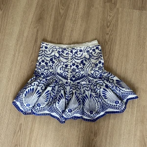 Kjol från Zara - Supersöt kort kjol från Zara med blått och vitt mönster. Kjolen har volang nertill och en markerad midja. Perfekt för sommarens alla tillfällen! Materialet känns lätt och luftigt. Aldrig använd! Pris kan diskuteras❤️