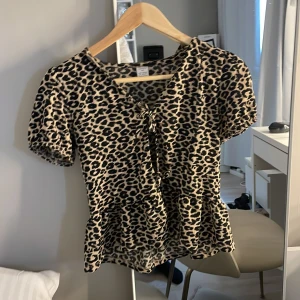 Leopardmönstrad topp från Lindex - Säljer en kortärmad topp från Lindex med leopardmönster. Toppen har knytning framtill och lätt volang nertill. Perfekt för dig som gillar djurmönster och vill ha en trendig look.