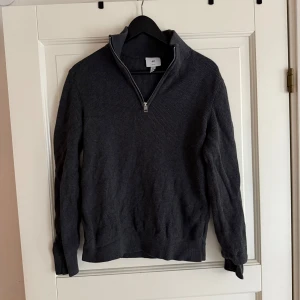  tröja med halv dragkedja från H&M - Säljer en mörkgrå stickad tröja från H&M med halv dragkedja och hög krage. Slim fit-modell som passar perfekt till lager-på-lager. Tröjan har långa ärmar och ribbade muddar vid ärmslut och nederkant.