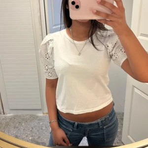 Vit tröja med broderade volangärmar - Säljer en söt vit croppad topp med puffiga kortärmar i broderad spets. Toppen har rund halsringning 