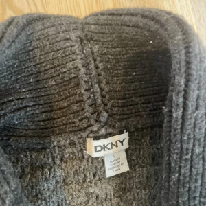 Mörkgrå stickad kofta från DKNY - Säljer en mysig mörkgrå stickad kofta från DKNY med knappar framtill och bred ribbad krage. Perfekt för lager-på-lager och har långa ärmar samt en mjuk känsla. Snygg till både jeans och kjol!