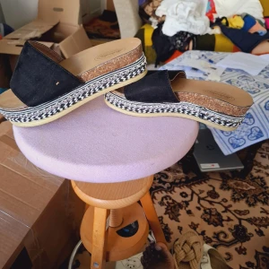 Svarta sandaler med platåsula - Säljer ett par svarta sandaler med bred rem i mocka och snygg platåsula med flätad detalj i svartvitt. Sulan har korkimitation och en ljus yttersula. Perfekta för sommaren och ger lite extra höjd.