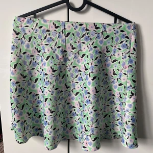 Blommig kjol i pastellfärger - Supersöt kjol med blommigt mönster i ljusgrönt, blått, lila och vitt. Kjolen har en lätt utsvängd form och är perfekt för dig som gillar färg och mönster. Tunn och skön, passar perfekt till varmare dagar. Är i storlek 34 men är väldigt stretchig så passar även flertal storlekar uppåt. Jätte fint och skönt satin material