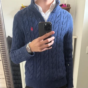 Blå kabelstickad tröja från Polo Ralph Lauren - Säljer en blå kabelstickad tröja från Polo Ralph Lauren med halv dragkedja och röd broderad logga på bröstet. Tröjan har hög krage och ribbade muddar vid ärmslut och nederkant. Perfekt för lager-på-lager och snygg till skjorta. Size S tts, fint skick något nopprig som går bort om man har ork. För frågor kom pm! /Neo💫