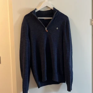 Mörkblå stickad tröja med dragkedja från Morris - Säljer en mörkblå stickad tröja från Morris med halv dragkedja och ribbad krage. Tröjan har långa ärmar och en liten broderad logga på bröstet. Perfekt för kyligare dagar och enkel att matcha med jeans eller chinos. Den är som helt ny. Det går att diskutera pris 