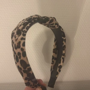 Leopardmönstrat diadem - Snyggt diadem med leopardmönster i beige och svart. Perfekt accessoar för att lyfta din outfit med en trendig touch. Diademet har en knut på ovansidan och är bekvämt att bära.