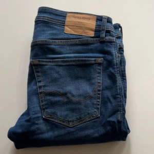 Blå slim straight jeans från Jack & Jones - Säljer ett par blå jeans från Jack & Jones i modellen Slim Straight/Tim. Jeansen har klassisk femficksdesign, slitningar på framsidan och en snygg läderpatch bak i midjan. Perfekta för dig som gillar en smal men rak passform.
