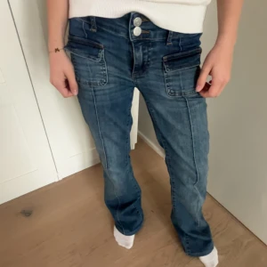 Blå jeansbyxor med raka ben och dubbla knappar - Snygga blå jeansbyxor med raka ben och dubbla knappar i midjan. Byxorna har stora fickor fram och bak samt markerade sömmar som ger en cool look. Perfekta till vardags för en avslappnad men trendig stil.