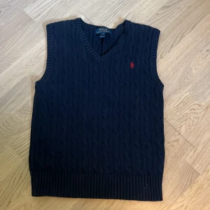 Mörkblå stickad väst Polo Ralph Lauren - Snygg mörkblå stickad väst från Polo Ralph Lauren med klassisk v-ringning och kabelstickat mönster. Jätte fin kvalité knappt använd storlek S