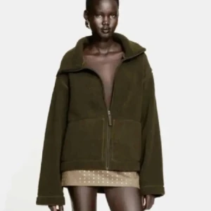 Olivgrön teddyjacka med dragkedja - Mysig olivgrön teddyjacka med oversized passform och stora fickor framtill. Jackan har hög krage och hel dragkedja, perfekt för kalla dagar. Materialet är fluffigt och ger en cool, avslappnad vibe. Passar dig som gillar streetstyle och vill hålla dig varm.