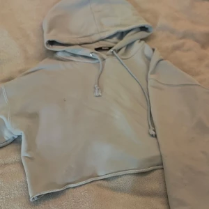 Ljusblå croppad hoodie från Bik Bok - Snygg ljusblå croppad hoodie från Bik Bok i storlek XS. Tröjan har huva med snörning och långa ärmar. Tillverkad i mjuk bomullsmix som är perfekt för chill dagar. Enkel design utan mönster och med rå kant nedtill för en trendig look. Tvättas självfallet innan den skickas, sminkfläckar samt små fläckar men inget som syns på💞