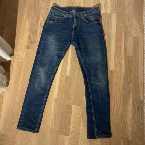 Blå jeans från Tiger of Sweden - Snygga blå jeans från Tiger of Sweden med klassisk femficksdesign och bruna detaljer vid linningen. Jeansen har en smal passform och raka ben, tillverkade i slitstarkt denimtyg. Perfekta för dig som gillar stilrena och tidlösa jeans. Det är skinny/slim fit jeans det beror på hur du är byggd