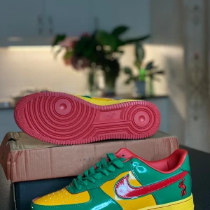 Nike Air Force 1 Concrete Boys färgglada - Nike Air Force 1 Concrete Boys i galet färgglad design med grönt, gult och rött lackat skinn. Röd sula, gröna skosnören och röda detaljer på häl och Swoosh. Broderad figur på sidan och texten 'CONCRETE BOYS' bak. Perfekta för dig som vill sticka ut.