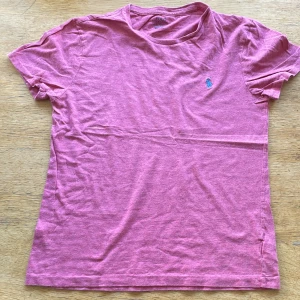 Rosa t-shirt från Polo Ralph Lauren - Snygg rosa t-shirt från Polo Ralph Lauren i custom slim fit. Klassisk design med korta ärmar och rund hals. På bröstet finns det ikoniska blå broderade Polo-loggan. Mjuk och skön bomull som passar perfekt till jeans eller shorts.