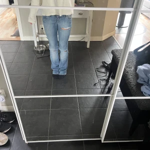 Ljusblå bootcut jeans med slitningar - Säljer ett par ljusblå jeans med bootcut passform och snygga slitningar vid knä och bakficka. Jeansen har låg midja och klassiska fem fickor. Perfekt för dig som gillar en avslappnad och trendig look. Midjemått rakt över 38 cm, innerbenslängd 85 