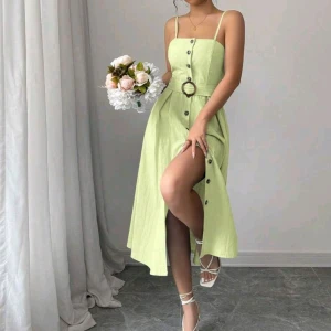 Ljusgrön klänning med knappar och bälte - Superfin ljusgrön långklänning med smala axelband, markerad midja och bälte med rund spänne. Klänningen har knappar framtill hela vägen ner och en snygg slits. Materialet ser ut som linne och modellen är ärmlös och luftig – perfekt för varma dagar.