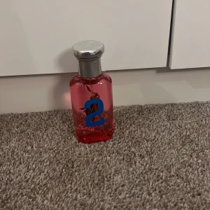 BIG PONY 2 WOMAN - Cool parfym från Ralph Lauren med genomskinlig rosa glasflaska, silverfärgat lock och tryck i blått och grönt. Flaskan har en stor siffra och den klassiska polospelaren på framsidan. Perfekt för dig som gillar färgstark design och vill sticka ut.