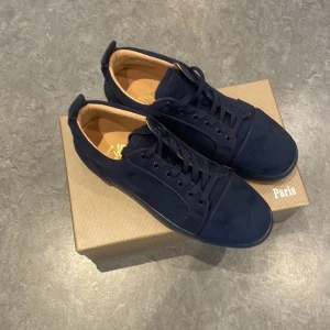 Mörkblå mockasneakers från Louboutin - Snygga mörkblå sneakers från Louboutin i mjuk mocka med rund tå och klassisk snörning. Skorna har en stilren design med diskreta sömmar och beige innersula. Perfekta för dig som vill ha en lyxig och clean look.