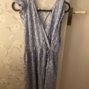 Blommig blå långklänning Kappahl S - endast använd 1 gång. Supersöt långklänning från Kappahl i storlek S. Klänningen är blå med vitt blommönster, omlottmodell med knyt i midjan och v-ringning. Perfekt för sommarens alla tillfällen och har en luftig känsla.