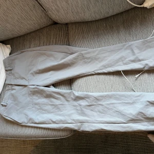 Ljusgrå kostymbyxor med rak passform - Snygga ljusgrå kostymbyxor med klassisk rak passform och hällor för bälte. Byxorna har en stilren look och är tillverkade i ett lätt tyg som känns bekvämt hela dagen. Perfekta för dig som gillar en clean och enkel stil. Bikbok