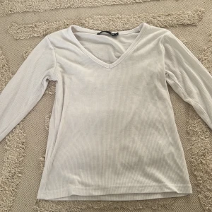 Vit ribbad långärmad tröja från lager157 - Vit långärmad topp från lager157 i ribbad bomull med v-ringning. Enkel och stilren modell som är lätt att matcha till olika outfits. Perfekt för dig som gillar basic-plagg med en snygg passform.