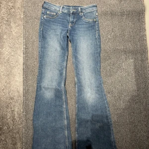 Blå bootcut jeans från H&M - Snygga lågmidjade jeans från H&M med klassisk femficksdesign och bootcut passform. Endast använda två gånger, och har inga defekter 