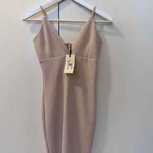 Beige kortklänning från Bik Bok XS oanvänd  - Supersnygg beige kortklänning från Bik Bok i storlek XS. Klänningen har smala axelband, v-ringad hals och figurnära passform. Materialet är mjukt och stretchigt, perfekt för dig som gillar minimalistisk stil. Dragkedja i ryggen för enkel påklädning.