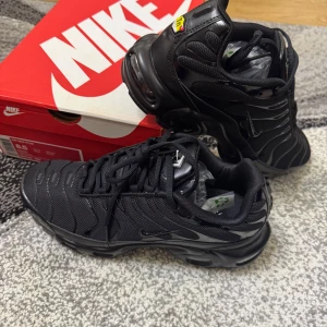 Nike Air Max Plus helsvarta sneakers - Nike Air Max Plus i helsvart med ikoniska Tn-detaljer och synlig Air Max-dämpning. Ovandel i mesh och syntet med vågformade linjer, robust yttersula och snörning. Perfekta för dig som gillar en sportig och clean look.